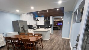 A modern kitchen with white cabinets, a central island, and a dining area with wooden chairs. - Newly Renovated, Charming 3-bedroom, 2-bathroom house in Arabi (Arabi)