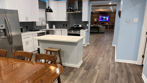A modern kitchen with white cabinets, a central island, and a dining area with a wooden table and chairs. - Newly Renovated, Charming 3-bedroom, 2-bathroom house in Arabi (Arabi)
