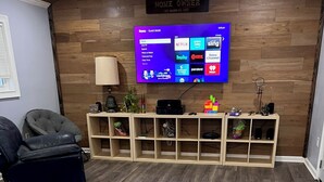 A modern living room with a flat-screen TV mounted on a wooden wall, a comfortable sofa, a wooden coffee table, and a built-in entertainment unit with shelves. - Newly Renovated, Charming 3-bedroom, 2-bathroom house in Arabi (Arabi)