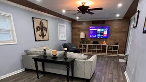 A modern living room with a grey sofa, a coffee table, and a ceiling fan. - Newly Renovated, Charming 3-bedroom, 2-bathroom house in Arabi (Arabi)