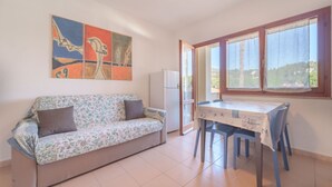Una habitación con sofá, una mesa y sillas. Hay un cuadro en la pared y una ventana con cortinas.