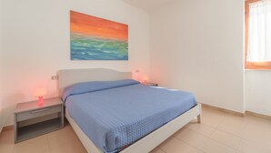 Un dormitorio con una cama, dos mesitas de noche, una lámpara de noche, un cuadro y una ventana con cortinas.