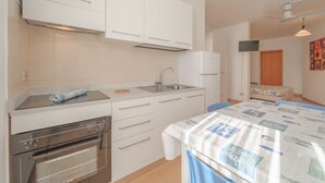 A compact kitchen with white cabinets, a built-in oven, and a sink. There is a small dining area with a table and chairs. - APPARTAMENTI GLI ORIZZONTI - ORIZZONTI N MONO 21 (Marina di Campo)