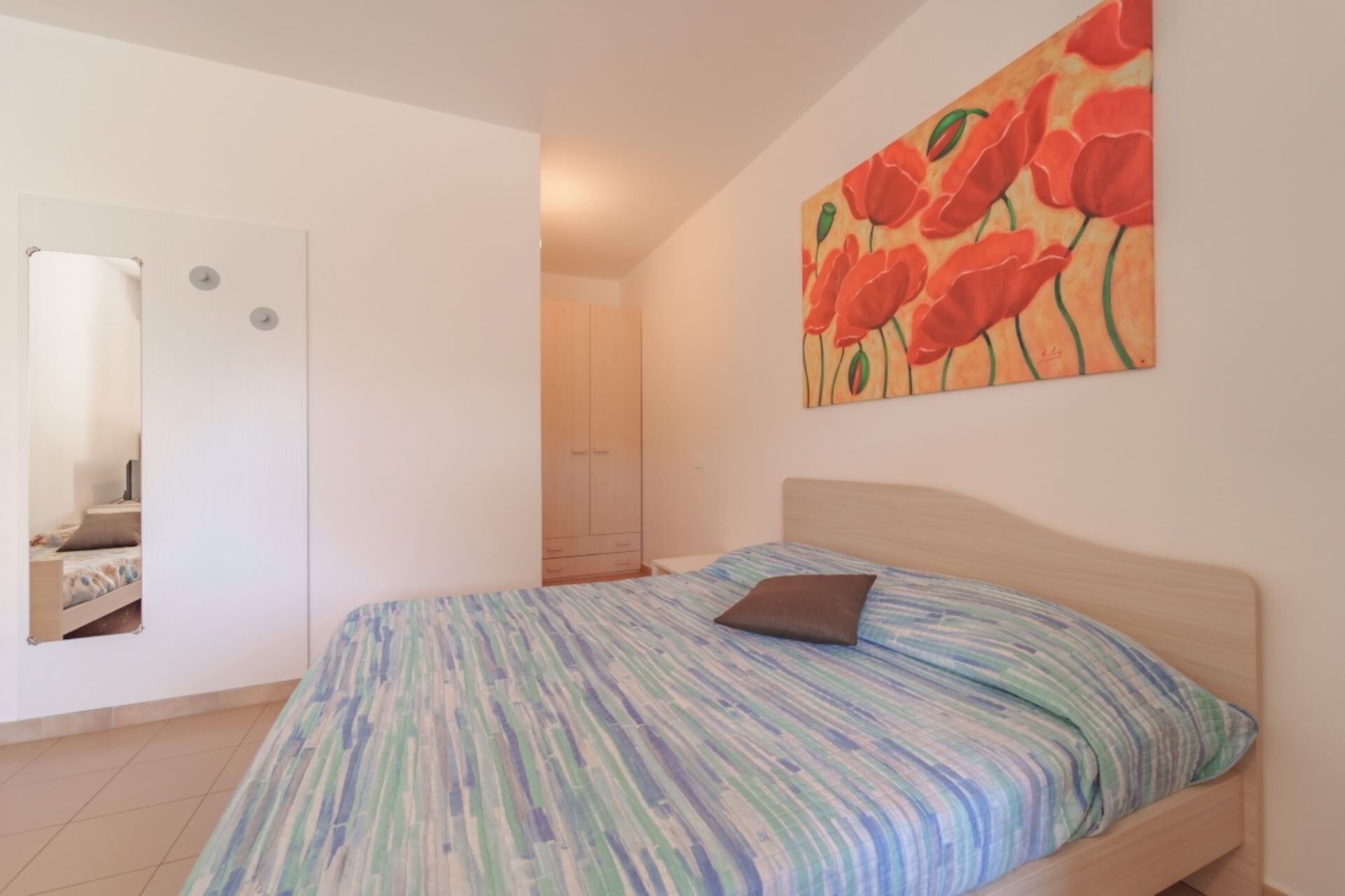 A bedroom with a bed, a painting, a wardrobe, and a mirror.