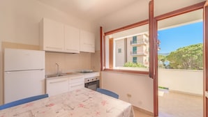 A compact kitchen with white cabinets, a built-in oven, and a dining table with a patterned tablecloth. - APPARTAMENTI GLI ORIZZONTI - ORIZZONTI N MONO 19 (Marina di Campo)