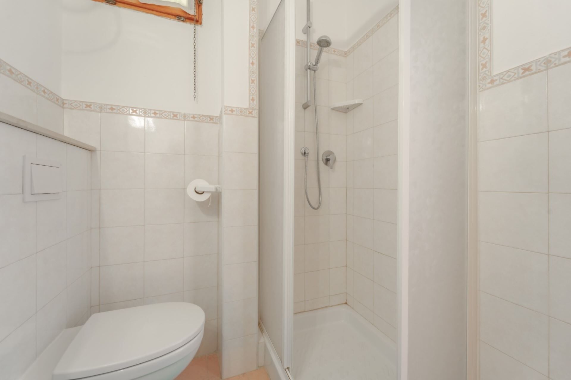 Une salle de bain équipée d’un WC, d’une douche avec un pommeau de douche amovible et d’un porte-rouleau de papier toilette.