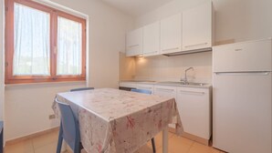A small kitchen with white cabinets, a refrigerator, a sink, and a table with a floral tablecloth. - APPARTAMENTI GLI ORIZZONTI - ORIZZONTI N MONO 15 (Marina di Campo)