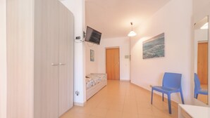 A room with a bed, a desk, a chair, a television mounted on the wall, and a door. - APPARTAMENTI GLI ORIZZONTI - ORIZZONTI N MONO 15 (Marina di Campo)