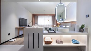 A modern bathroom with a large mirror, a sink, and a vanity. There is a television on a stand to the left and a plant on the vanity. - SYYF Xiang Shan You Yue Jiudian Guilin (Guilin)