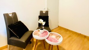 Ein kleiner Raum mit Massagesessel, einem kleinen Tisch mit Blumenvase und einer weißen Tür.