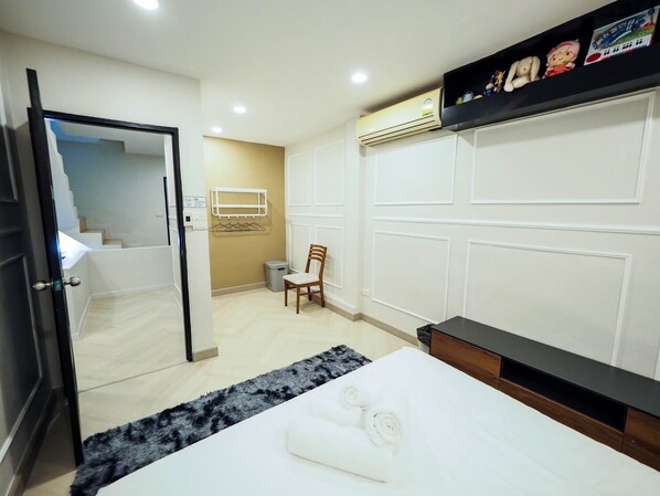 Habitación de hotel con cama, una silla, una mesita, un estante con juguetes y una escalera que lleva a otra habitación.