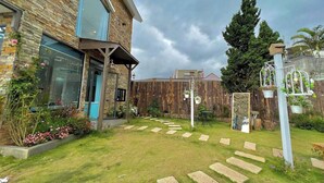 Una casa moderna con fachada de piedra, un jardín cuidado con piedras y una cerca de madera.
