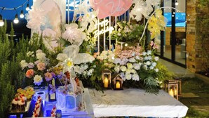 Un montaje para comer al aire libre con arreglos florales, un pastel con forma de corazón y un cartel que dice 'Happy Birthday'.