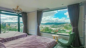 Habitación de hotel con dos camas, vista panorámica de la ciudad, una araña y una pequeña mesa con una silla.