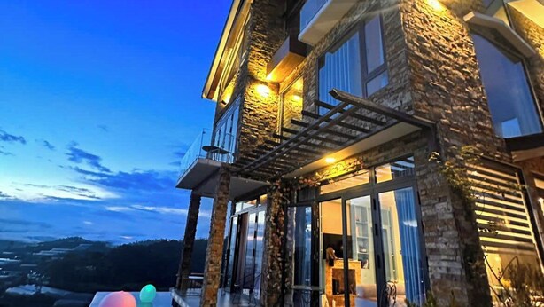 Una casa moderna con fachada de piedra, ventanas grandes y un área de piscina con barandilla de vidrio.