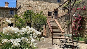 Edificio de piedra con una escalera que conduce a una puerta, rodeado de flores blancas y vegetación.