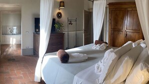 Un dormitorio con una cama grande, ropa de cama blanca, un armario de madera, una mesita de noche con una lámpara y vistas a la cocina.