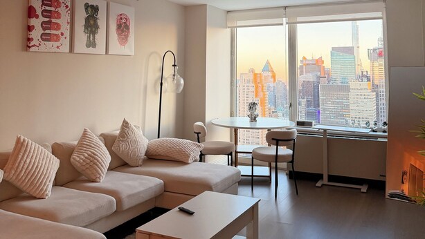 Un salon moderne comprenant un canapé, une table basse et un coin repas avec une table et des chaises. Une grande fenêtre offre une vue sur la ville.