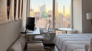 Une chambre d’hôtel avec vue sur la ville, un bureau avec un ordinateur, une chaise blanche, un lit et une petite table.