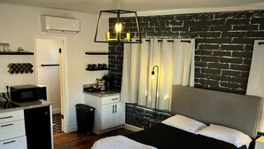 Een moderne slaapkamer met een groot bed, een houten kist, een kitchenette en een bakstenen muur.
