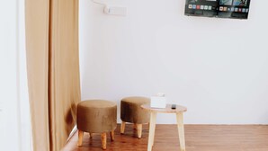 Une pièce comprenant deux poufs ronds de couleur marron, une petite table en bois sur laquelle se trouve un objet blanc, et un écran fixé au mur qui affiche différents contenus.