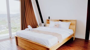 Un lit en bois avec une literie blanche, dans une pièce dotée d’une grande fenêtre et de rideaux.