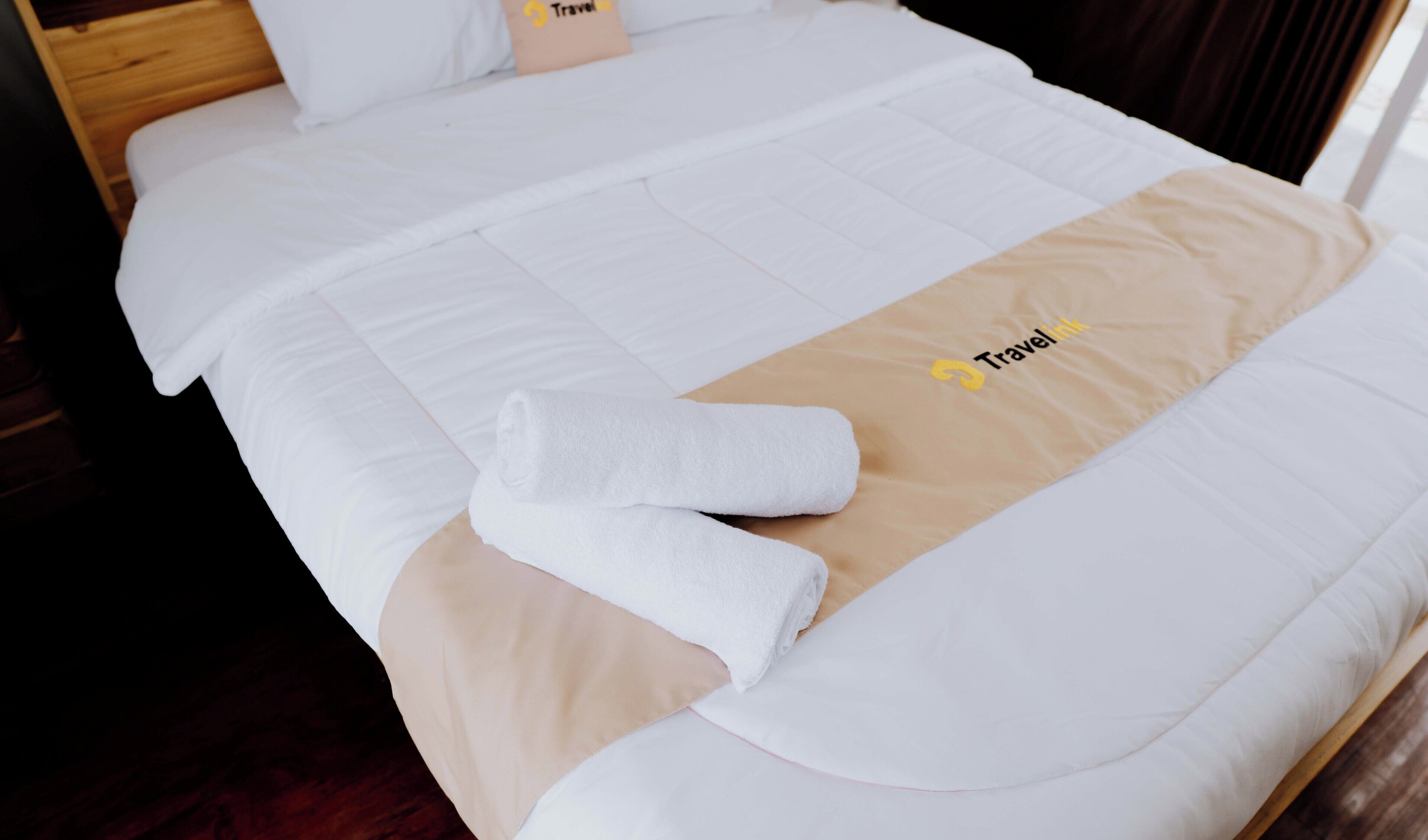 Una cama bien hecha con una toalla Travelink y una manta color beige.