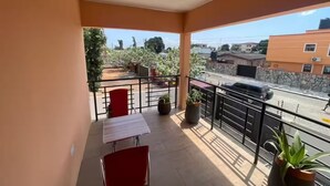 Un balcon avec une table et des chaises, des plantes en pot et une vue sur une rue et des immeubles.