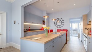 A modern kitchen with a central island, pendant lighting, and a large wall clock. - Portpatrick House by Interhome (Portpatrick)