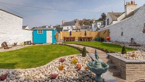 A residential backyard with a blue shed, a stone fountain, and a well-maintained lawn. - Portpatrick House by Interhome (Portpatrick)
