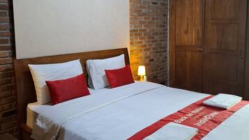 A hotel room with a bed, a brick wall, wooden doors, and a nightstand with a remote control and water bottles.
