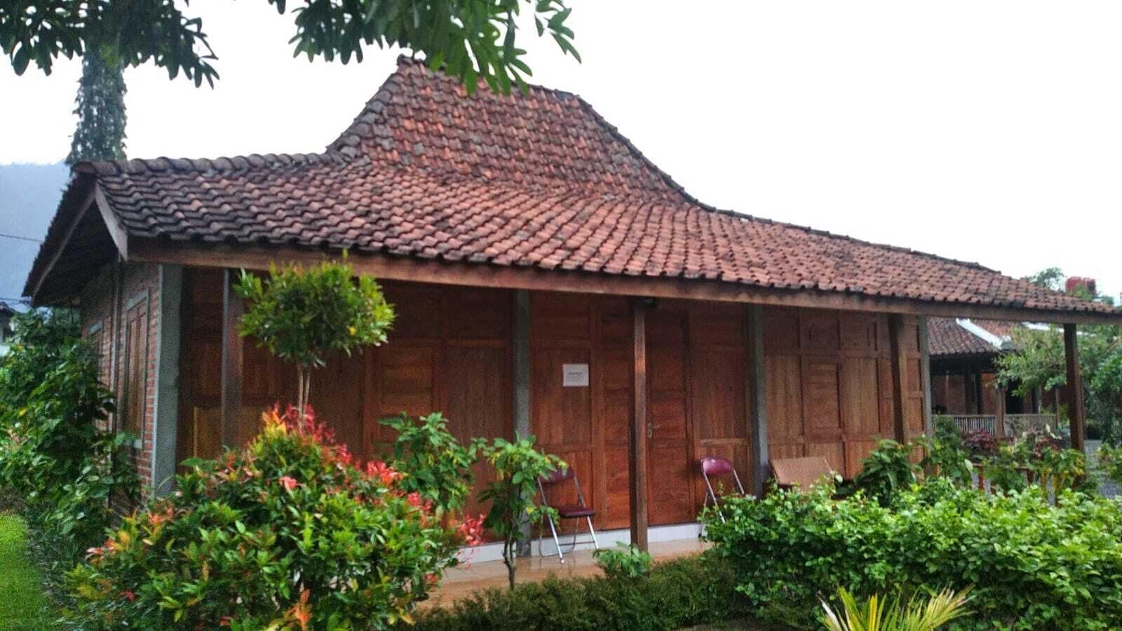 Ein traditionelles Holzhaus mit Ziegeldach, umgeben von üppigem Grün und einer kleinen Veranda mit Stühlen.