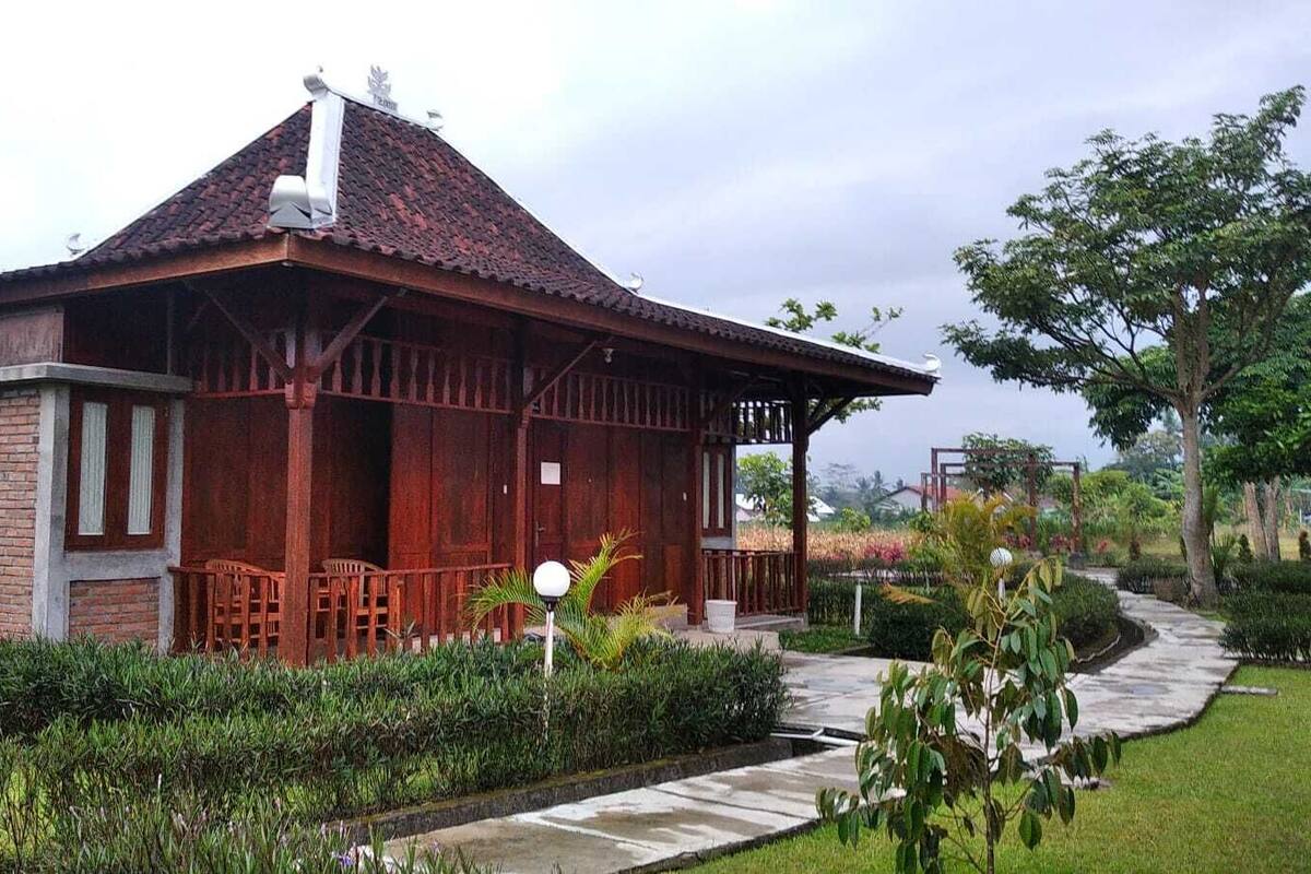 A wooden building with a tiled roof, surrounded by a well-maintained garden with a pathway leading to it.