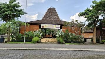 A traditional building with a tiled roof, surrounded by greenery and a paved entrance area.