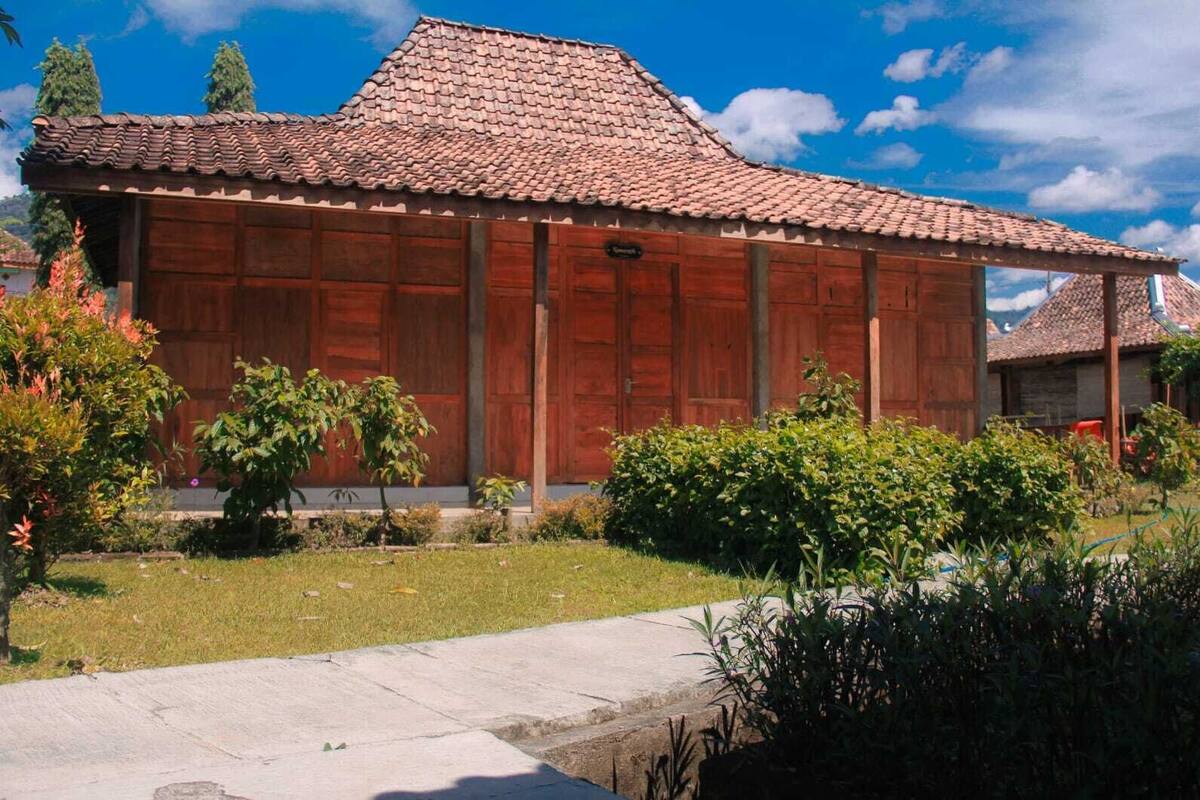 A traditional wooden building with a tiled roof, surrounded by well-maintained gardens and a clear blue sky.