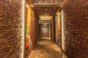 A hallway with stone flooring and brick walls, leading to a door at the end.