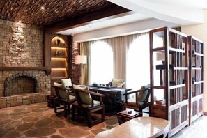A stone-floored room with a fireplace, a dining table with chairs, and a bookshelf.