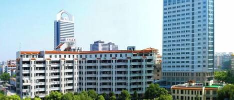 A multi-story hotel with a flat roof, surrounded by greenery and other buildings.