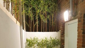 A narrow outdoor space with artificial green turf, bamboo plants, and a brick wall.