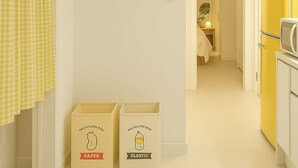 A kitchen with a yellow refrigerator, a smiley face wall art, and recycling bins labeled 'paper' and 'plastic'.