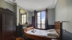 Ein Schlafzimmer mit einem hölzernen Bett, einem Schminktisch, einem Spiegel und einem Fenster mit Vorhängen.