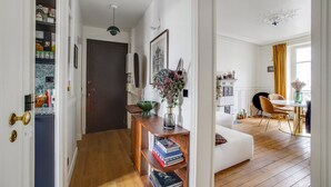 Ein geräumiges Wohnzimmer mit weißem Sofa, Holzboden, einem Essbereich mit Tisch und Stühlen sowie einem Bücherregal voller Bücher.