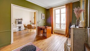 Ein Zimmer mit Holzboden, einem Essbereich mit Stühlen und einem Tisch, einem Kamin mit einer Vase und einem Fenster mit Vorhängen.