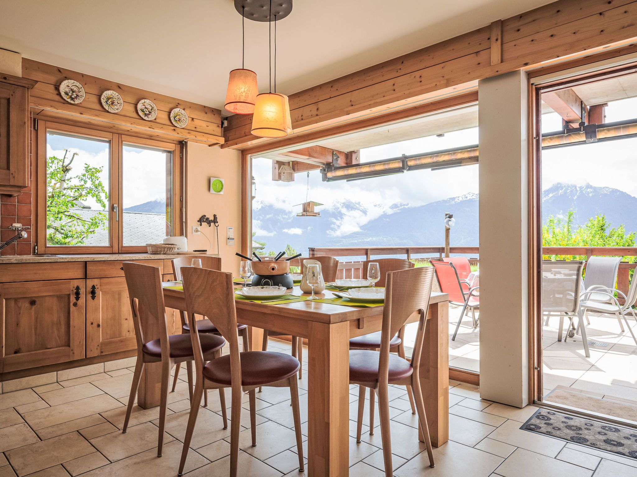 Un intérieur en bois avec une table à manger pour quatre personnes, de grandes fenêtres offrant une vue sur les montagnes et un coin cuisine doté de meubles en bois.