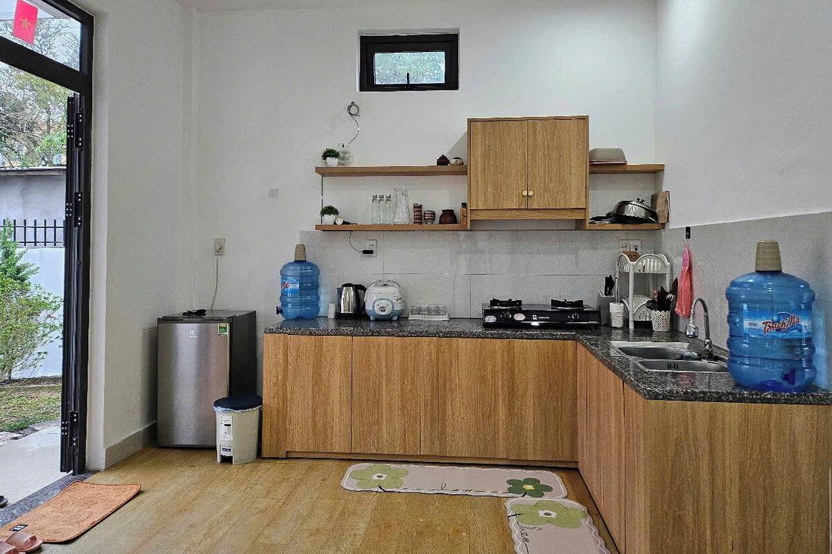 A compact kitchen with wooden cabinets, a built-in oven, a sink, and a window with a view of greenery outside.