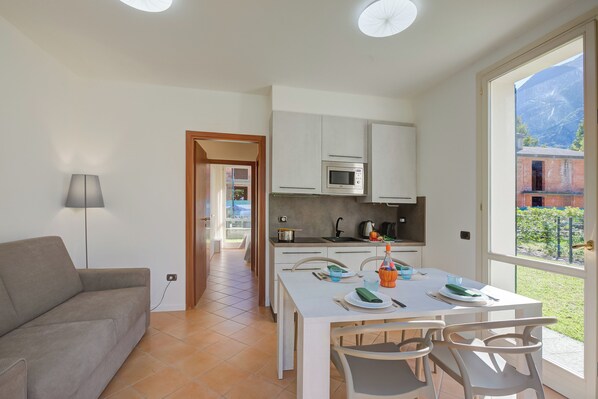 A modern kitchen with white cabinets, a microwave, and a dining area with a table and chairs. - Porto Letizia Ortensia 1, Porlezza, Italy (Porlezza)