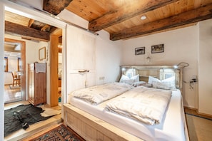 A bedroom with a wooden ceiling, a double bed, a bedside table, and a wardrobe.
