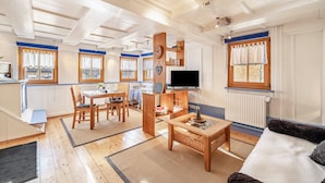 Una sala de estar moderna con comedor, muebles de madera, un televisor de pantalla plana y un amplio ventanal con cortinas.