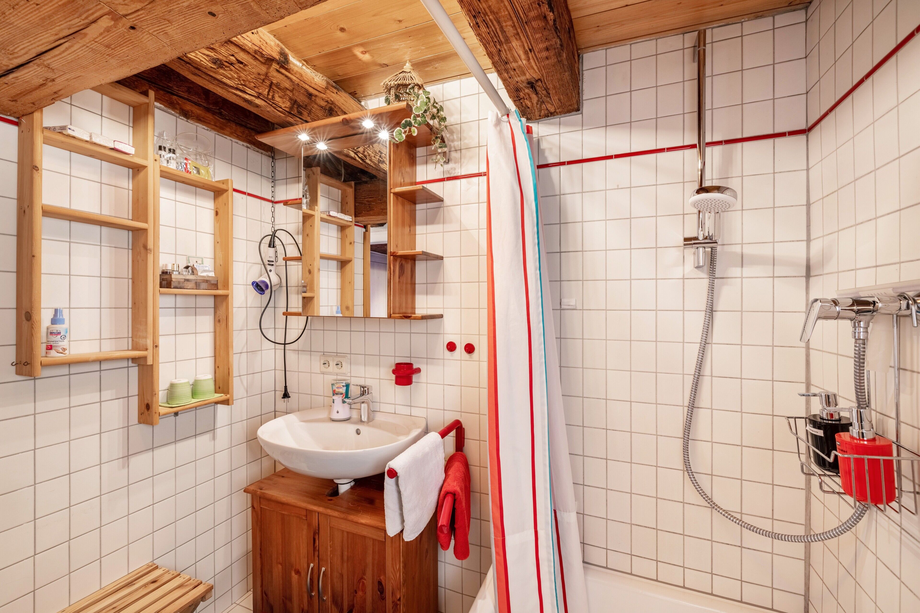 A bathroom with a wooden vanity, a sink, a shower with a handheld showerhead, and a towel rack.