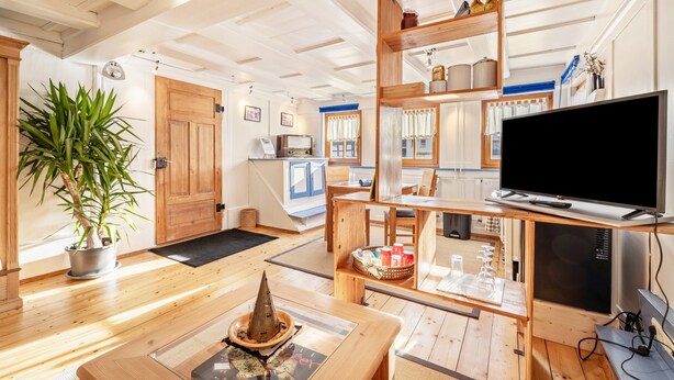 Una sala de estar moderna con pisos de madera, un televisor, una planta en maceta y un comedor con mesa y sillas.